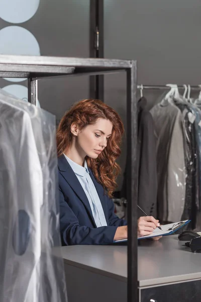 Junge attraktive Managerin schreibt in Klemmbrett am Arbeitsplatz mit POS-Terminal — Stockfoto