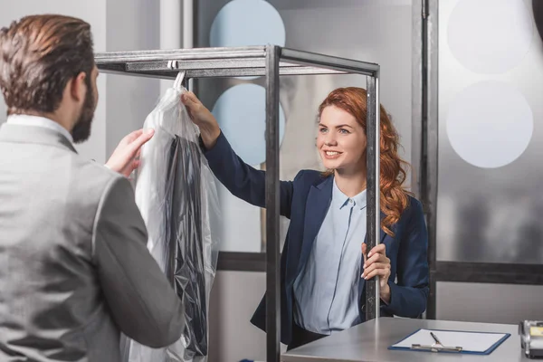 Happy young dry cleaning manageress giving bag of clothes for customer — Stock Photo