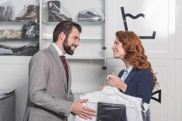 Dry cleaning manageress giving bag with clothes to happy man — Stock Photo