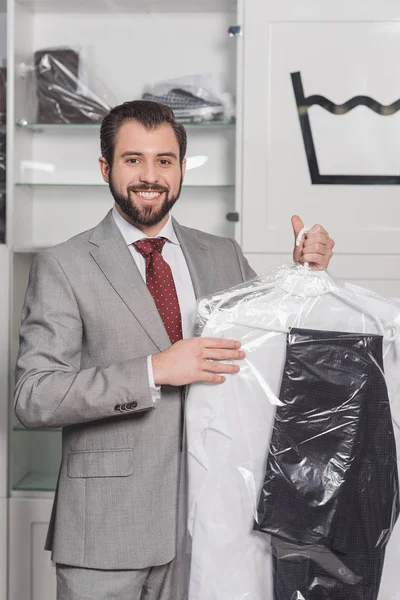 Businessman holding plastic bag of clean clothing at dry cleaning — Stock Photo