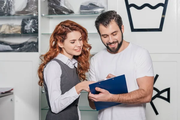 Handsome dry cleaning manager writing order of young woman — Stock Photo