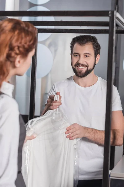 Handsome young dry cleaning manager giving clothes to customer — Stock Photo