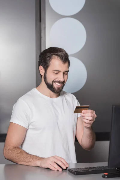 Handsome young manager sitting at workplace with gold credit card — Stock Photo