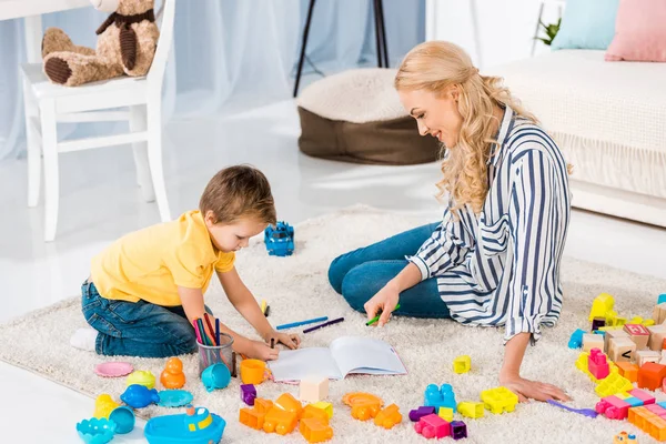 Giovane madre che aiuta il figlio mentre disegna insieme a casa — Foto stock