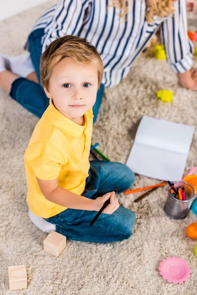 Selective focus of little boy looking at camera while drawing picture together with mother at home — Stock Photo