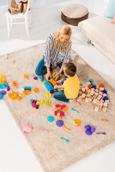 Высокий угол зрения матери и маленького сына, играющих вместе с игрушками на полу дома — стоковое фото