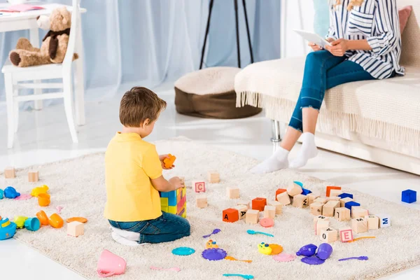 Plan recadré de la femme en utilisant une tablette tout petit fils jouant avec des jouets à la maison — Photo de stock
