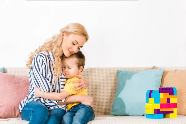 Sensual mother and little son hugging each other while resting on sofa at home — Stock Photo