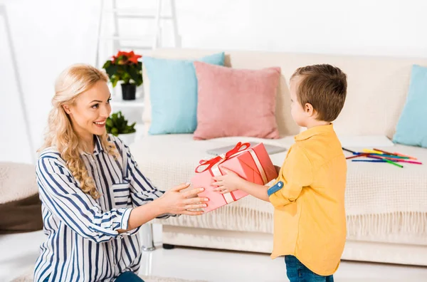 Mãe sorridente presenteando o pequeno filho em casa — Fotografia de Stock