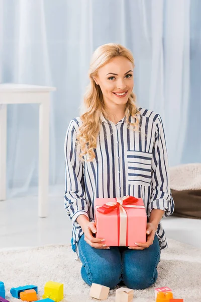 Portrait of happy woman with wrapped gift in hands looking at camera at home — Stock Photo