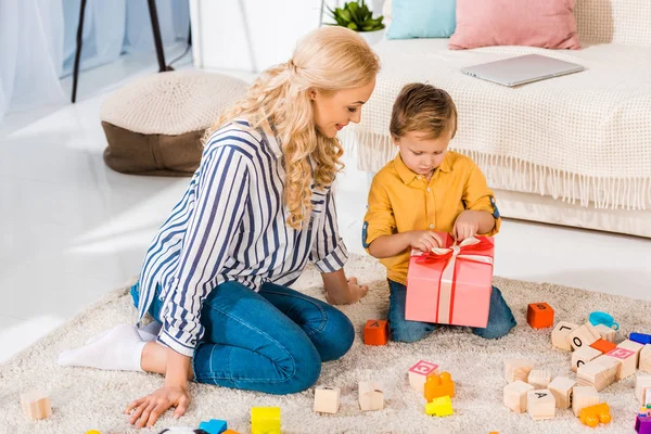 Little boy opening wrapped gift from mother at home — Stock Photo