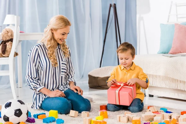 Little boy opening wrapped gift from mother at home — Stock Photo