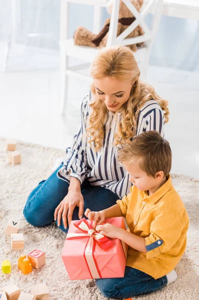 Маленький мальчик открывает завернутый подарок от мамы дома — стоковое фото
