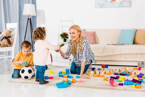 Madre feliz y los niños jugando con bloques de plástico - foto de stock