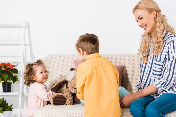 Lächelnde Mutter schaut, wie Tochter und Sohn mit Teddybär spielen — Stockfoto