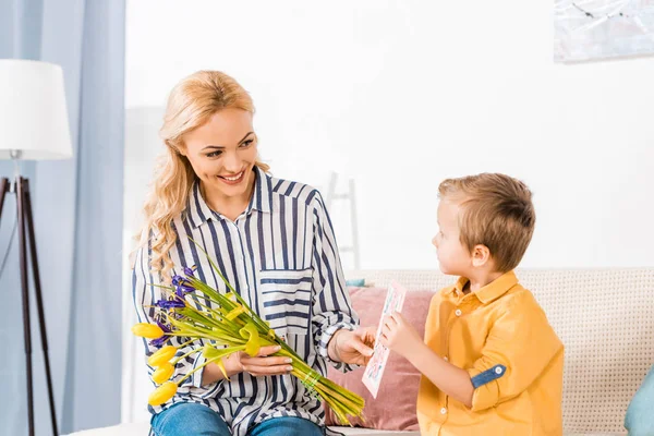 Entzückender Sohn schenkt Mutterstrauß und Postkarte zum Muttertag — Stockfoto