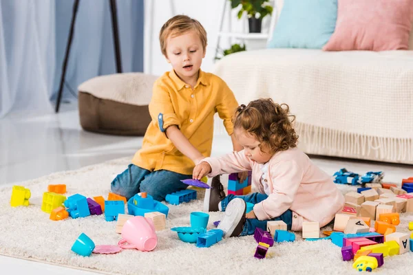 Irmãos adoráveis brincando com blocos de plástico no chão — Fotografia de Stock