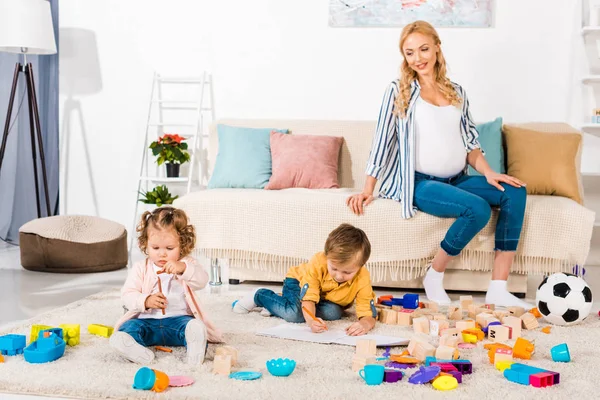 Smiling pregnant woman looking how children playing on floor — Stock Photo