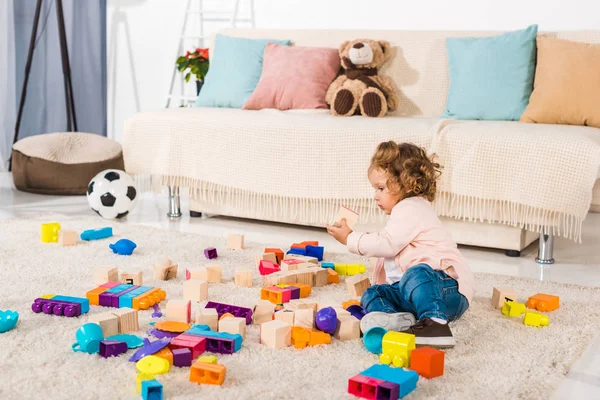 Entzückendes Kind spielt mit Holzwürfeln und Plastikklötzen auf dem Boden — Stockfoto