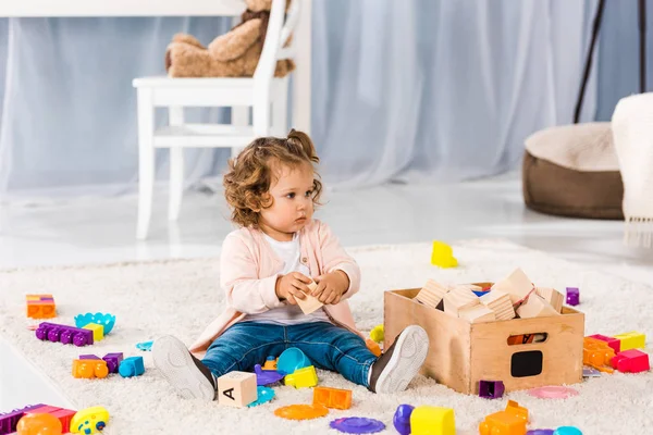 Entzückendes kleines Kind sitzt auf Teppich und spielt mit Spielzeug — Stockfoto