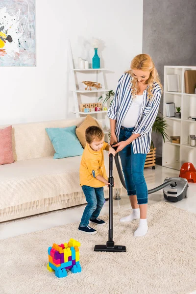 Feliz embarazada mujer con lindo pequeño hijo limpieza alfombra con aspiradora juntos - foto de stock