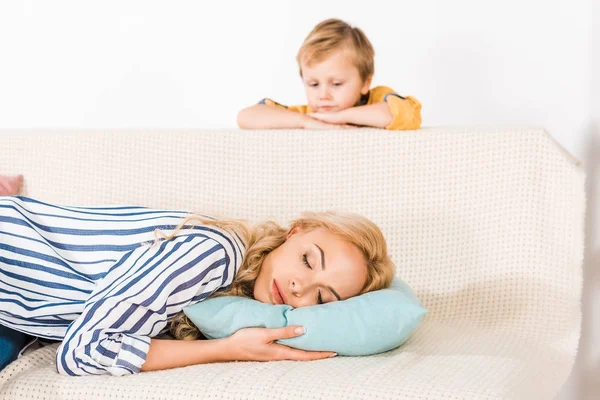 Netter kleiner Junge schaut Mutter an, die zu Hause auf dem Sofa schläft — Stockfoto