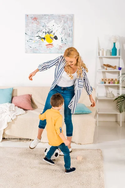 Mãe alegre e pequeno filho brincando com bola de futebol em casa — Fotografia de Stock