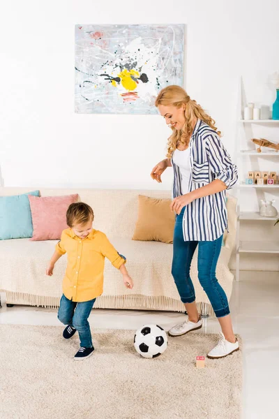 Feliz madre e hijo pequeño jugando con pelota de fútbol en casa - foto de stock