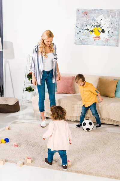 Allegra madre e simpatici bambini piccoli che giocano con il pallone da calcio a casa — Foto stock