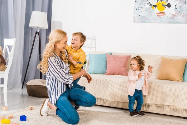 Красивая счастливая мать и красивые маленькие дети, играющие вместе дома — стоковое фото