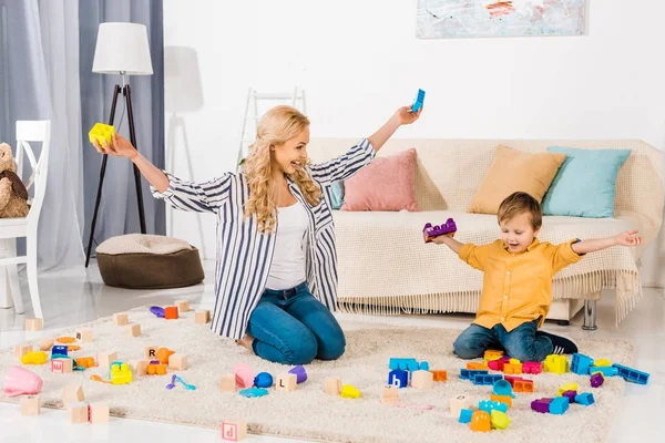 Счастливые мать и сын играют с цветными блоками дома — стоковое фото