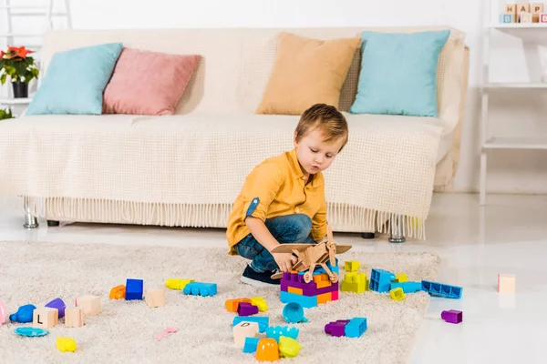 Adorabile bambino che gioca con aeroplano giocattolo e blocchi colorati a casa — Foto stock