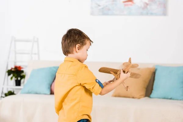 Pequeno menino adorável brincando com avião de brinquedo de madeira em casa — Fotografia de Stock