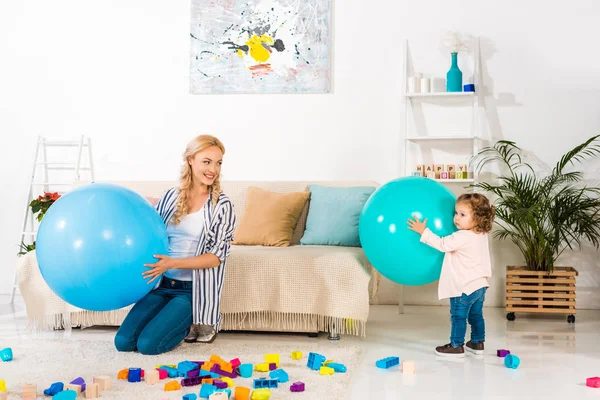 Bela mãe feliz e filha infantil brincando com bolas de fitness e blocos coloridos em casa — Fotografia de Stock