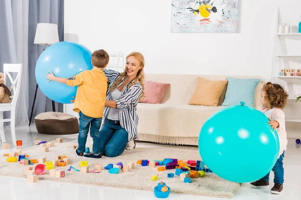 Feliz madre y niños jugando con pelotas de fitness y bloques de colores en casa - foto de stock