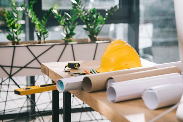 Hardhat, tape measure and blueprints on table in modern architect office — Stock Photo