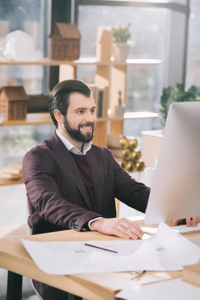 Handsome architect sitting at workplace with computer and blueprints — Stock Photo