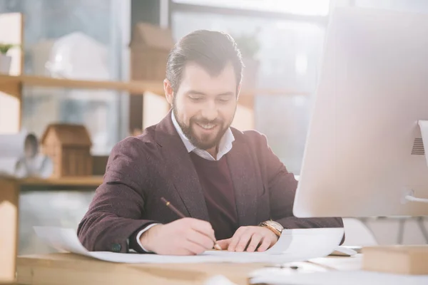Handsome architect drawing blueprint at workplace with computer — Stock Photo