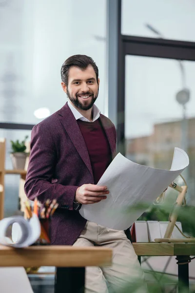 Smiling architect looking at blueprint in modern office — Stock Photo