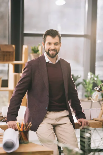 Усміхнений архітектор стоїть на робочому місці в сучасному офісі — стокове фото