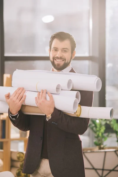 Smiling architect holding pile of blueprints in modern office with backlit — Stock Photo