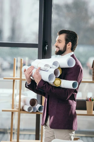 Arquiteto sorrindo segurando pilha de plantas no escritório moderno — Fotografia de Stock