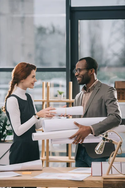 Arquitectos multiétnicos que trabajan con planos en oficinas modernas - foto de stock