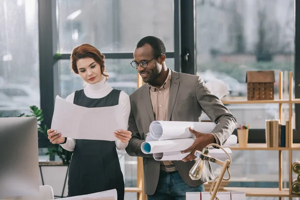 Arquitectos multiétnicos que trabajan con planos en el lugar de trabajo - foto de stock