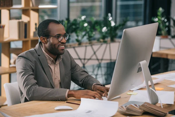 Architetto afroamericano che lavora con computer e cianografie in ufficio — Foto stock