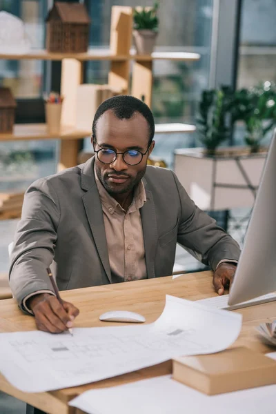 Afrikanisch-amerikanischer Architekt mit Brille arbeitet mit Computer und Bauplänen im Büro — Stockfoto