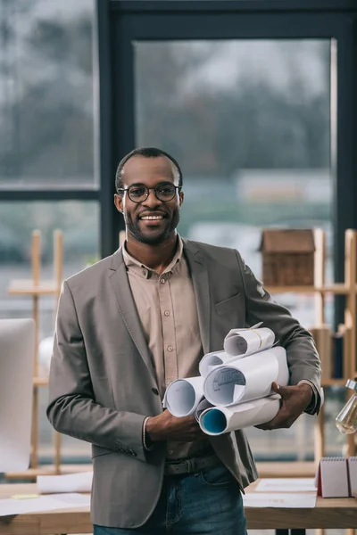 Fröhlicher afrikanisch-amerikanischer Architekt mit Bauplänen im Amt — Stockfoto