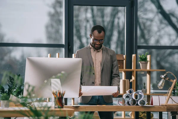 Arquiteto afro-americano trabalhando com plantas no local de trabalho com computador — Fotografia de Stock