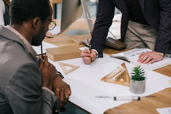 Cropped view of multiethnic architects discussing and drawing blueprints in modern office — Stock Photo