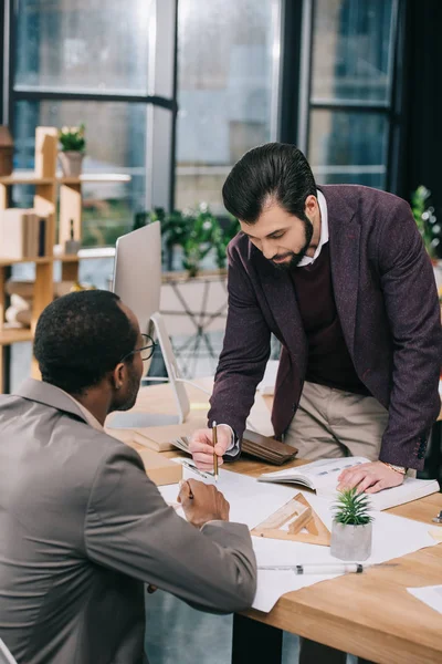 Multiethnic architects discussing and drawing blueprints in modern office — Stock Photo